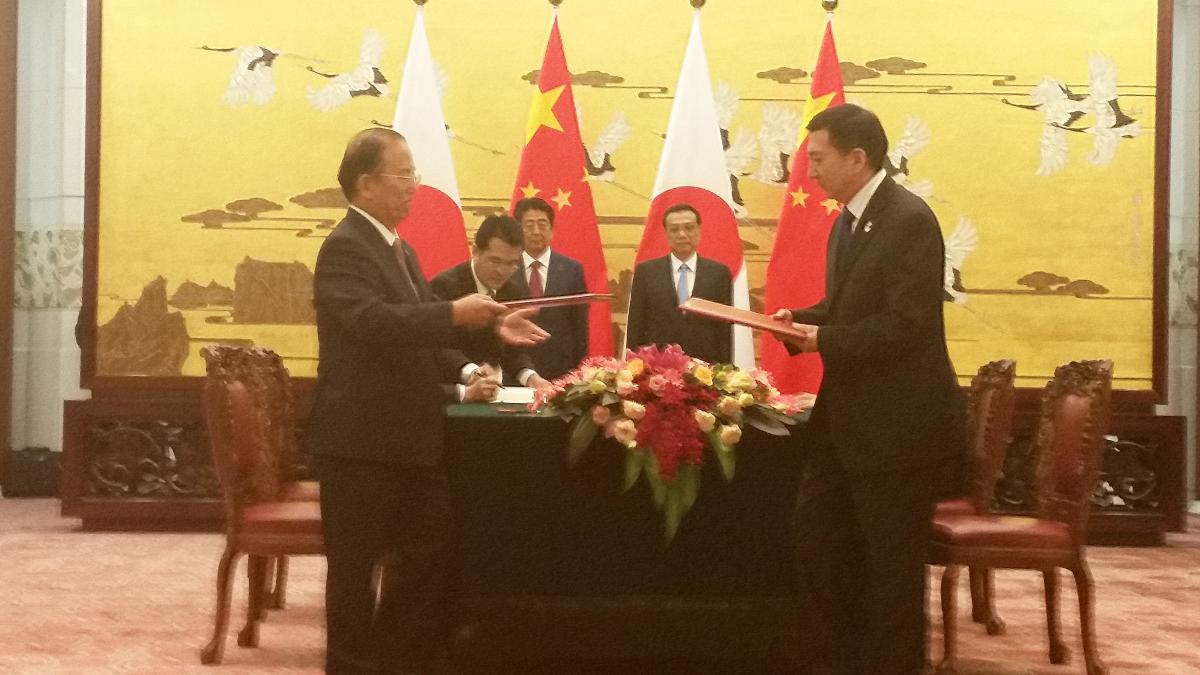 Beijing 2022 and Tokyo 2020 men in suits in a room exchanging documents