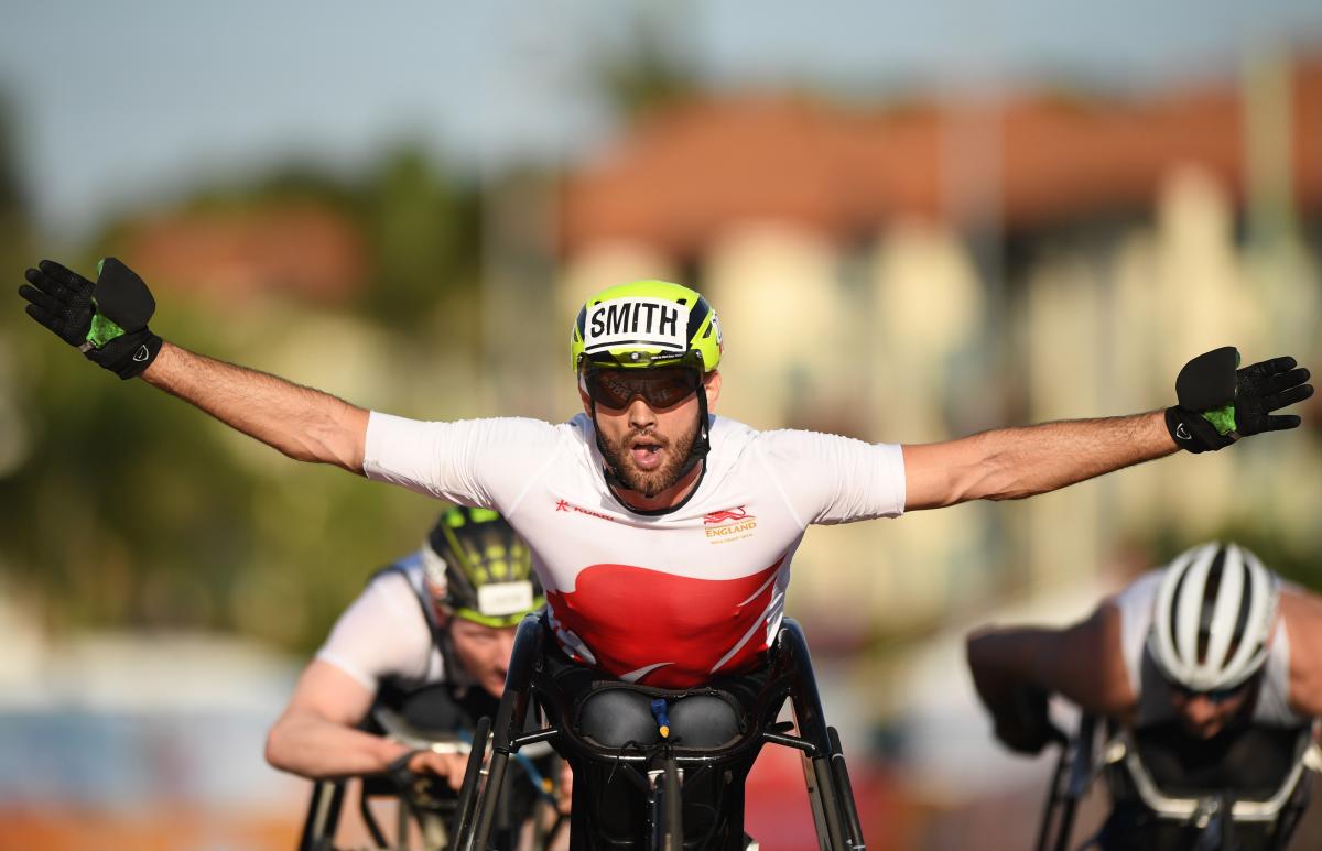 male wheelchair racer Johnboy Smith raises his arms wide as he crosses the finish line
