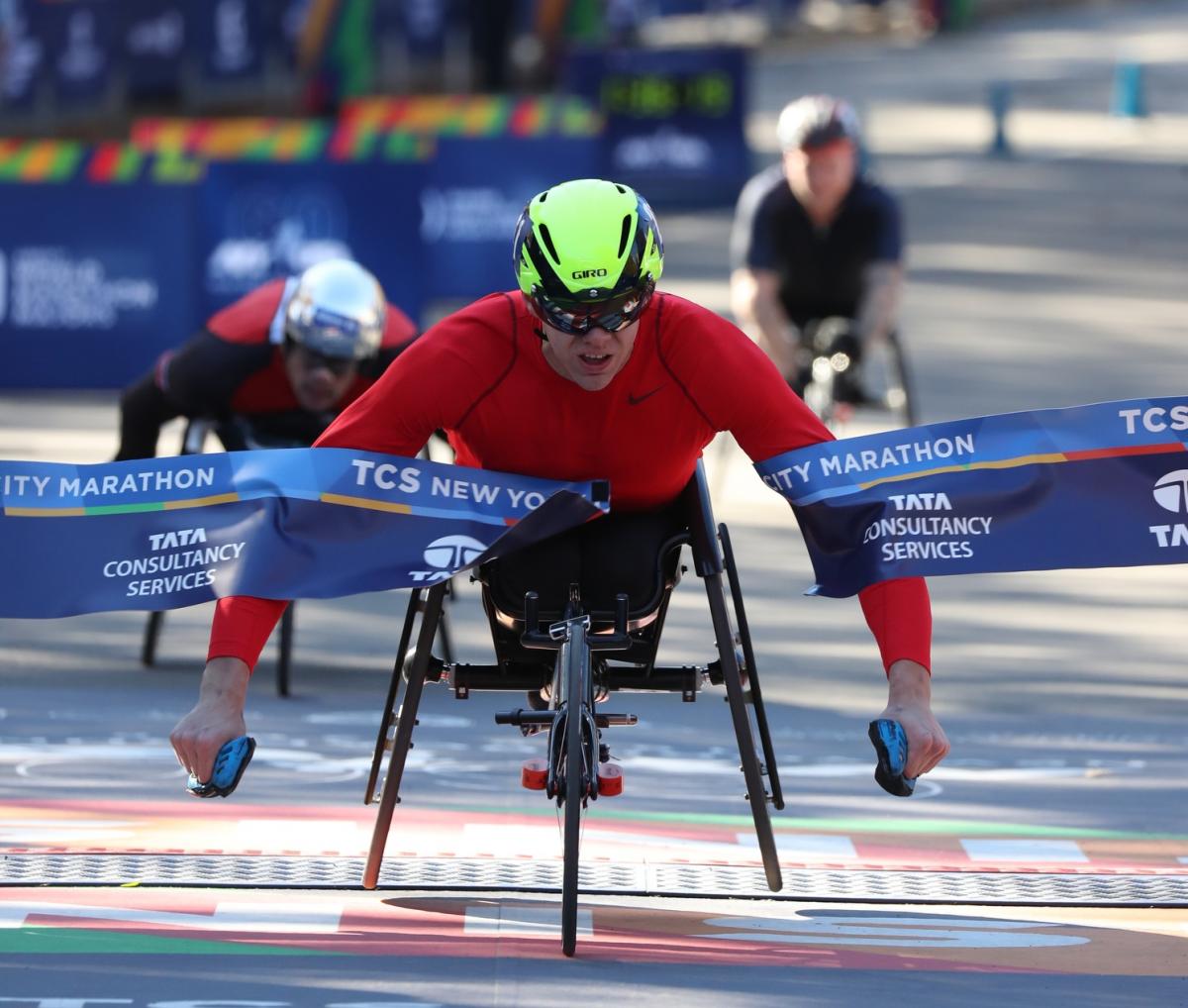 male wheelchair racer Daniel Romanchuk breaks the tape on the finish line ahead of two other wheelchair racers