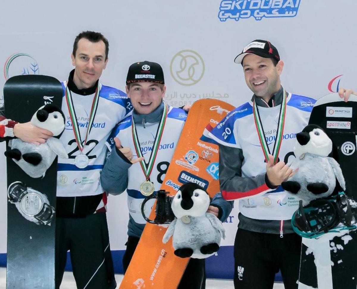 Chris Vos - Netherlands - Dubai 2018 World Para Snowboard World Cup Three men with helmets in an indoor snowboard track
