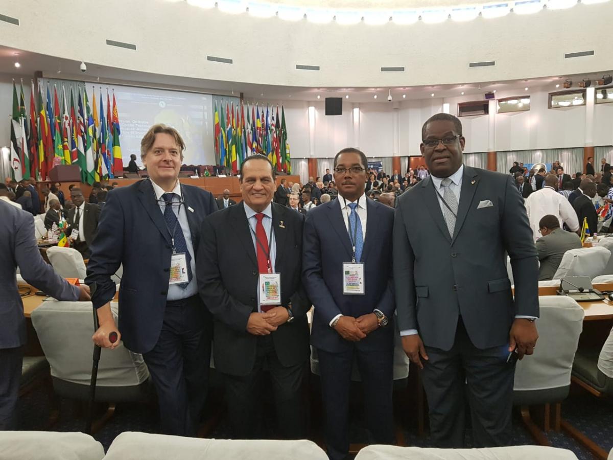 APC President Leonel da Rocha Pinto four men including Leonel da Rocha Pinto standing in suits in a conference hall