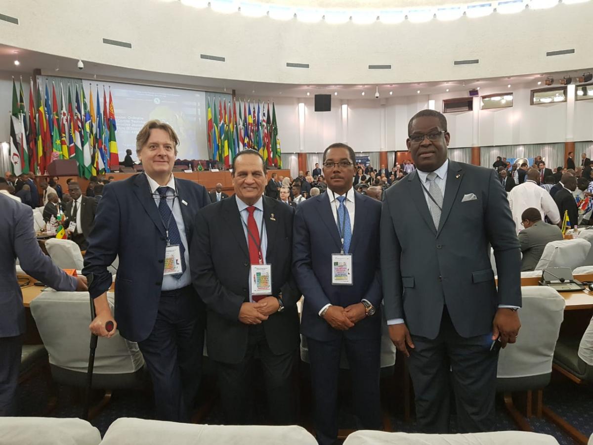 four men including Leonel da Rocha Pinto standing in suits in a conference hall