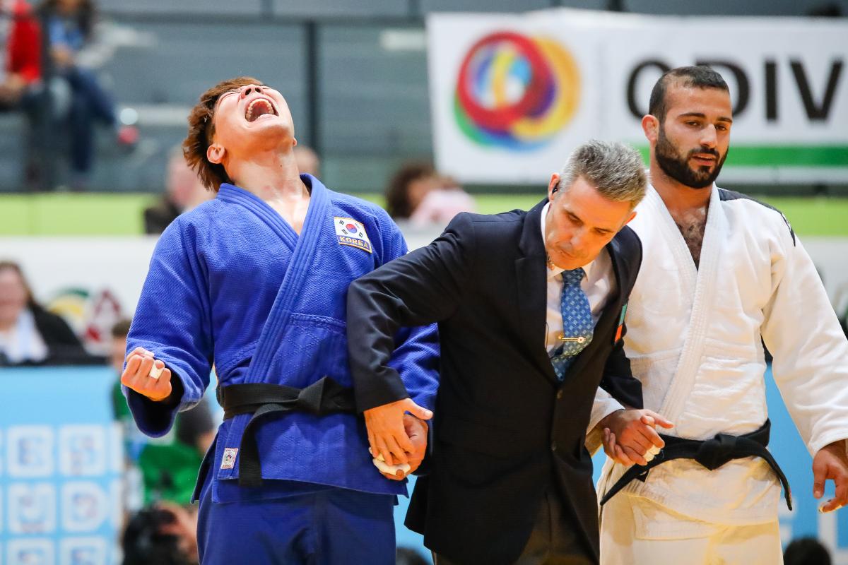 A men in suit holding the hands of two men in judo kimonos