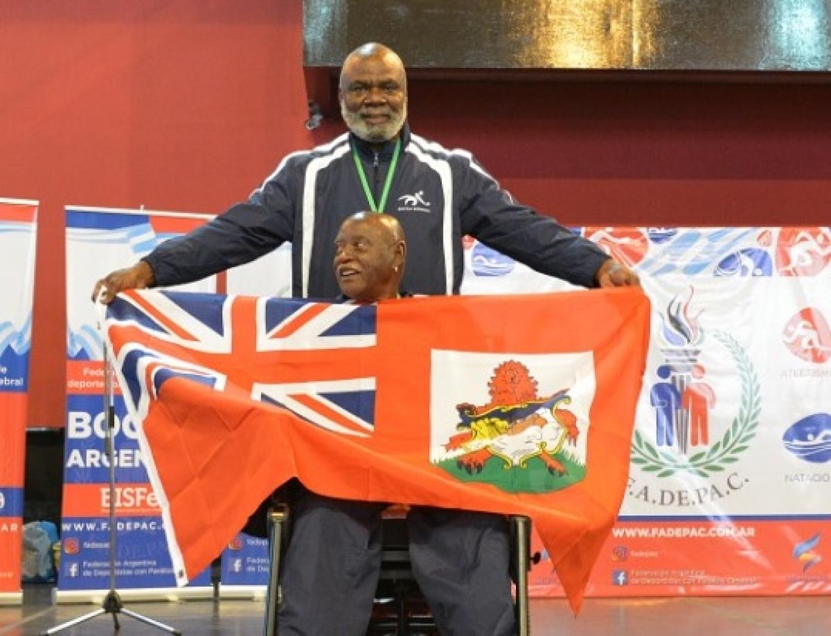 male boccia athlete Steve Wilson on the podium holding up a Bermuda flag