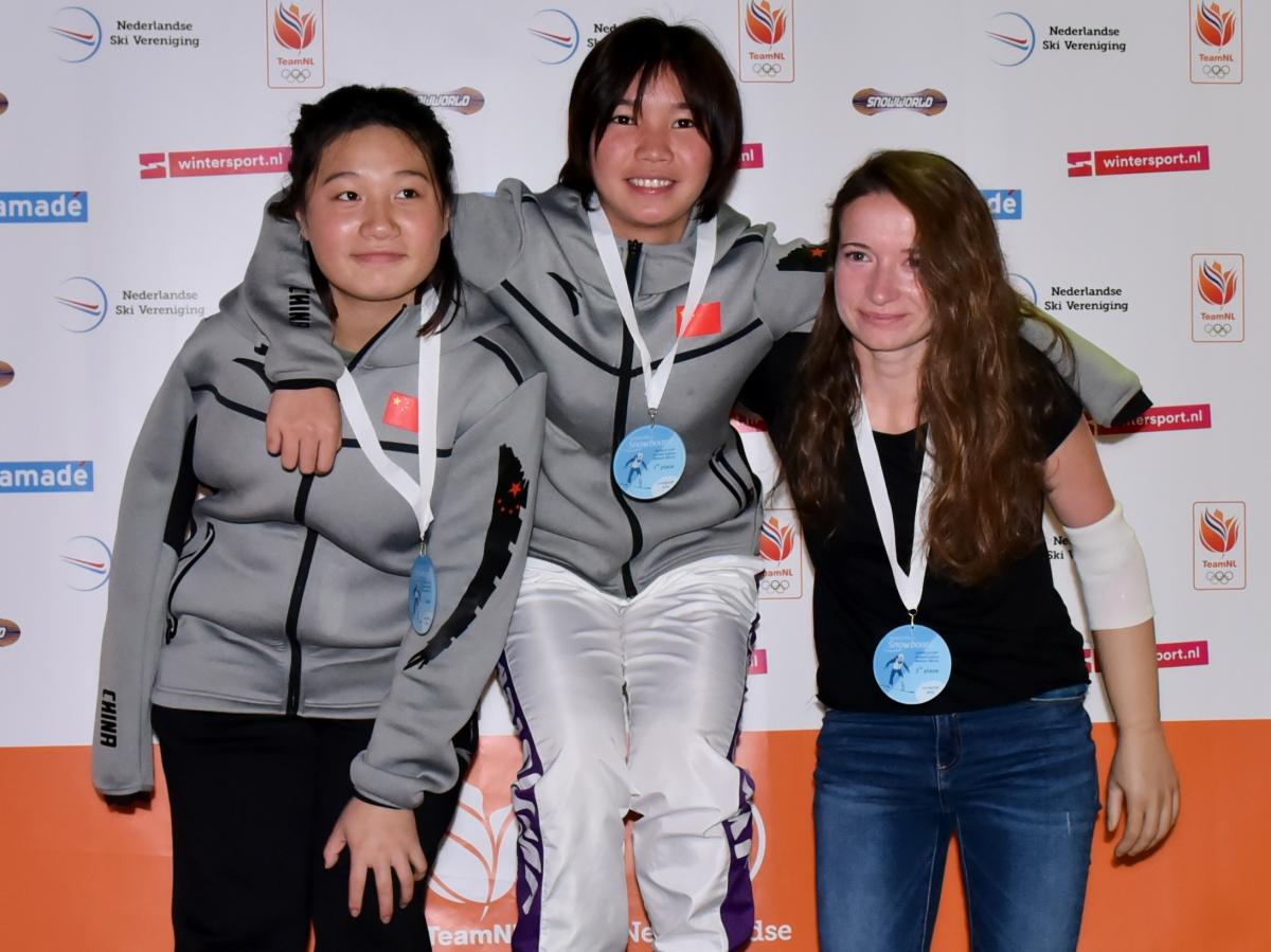 three female snowboarders standing on the podium with their arms around eachother