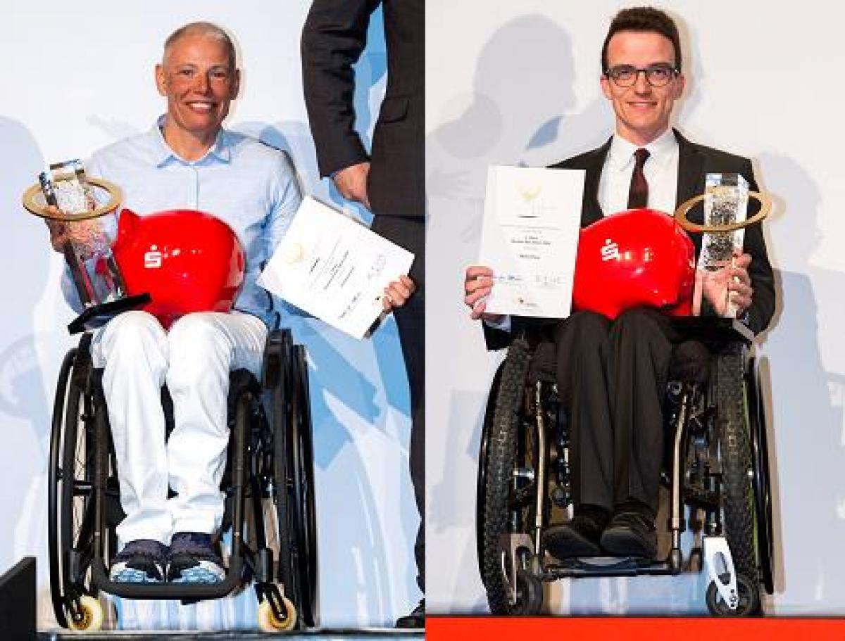 A woman and a man in wheelchairs holding a trophy and a certificate