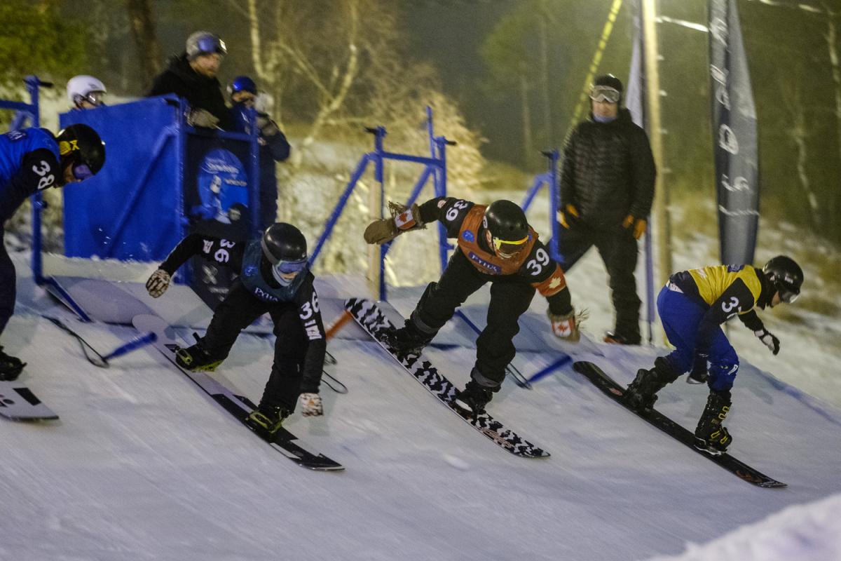 Four male snowboarders at the start gate for snowboard-cross