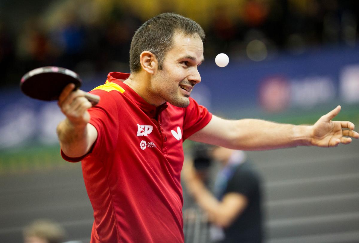 male Para table tennis player Jordi Morales raises his arms at the table 