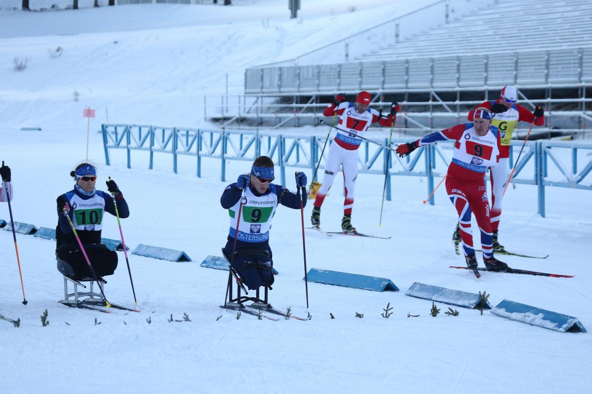 A group sitting and standing skiers competing in a Para biathlon race