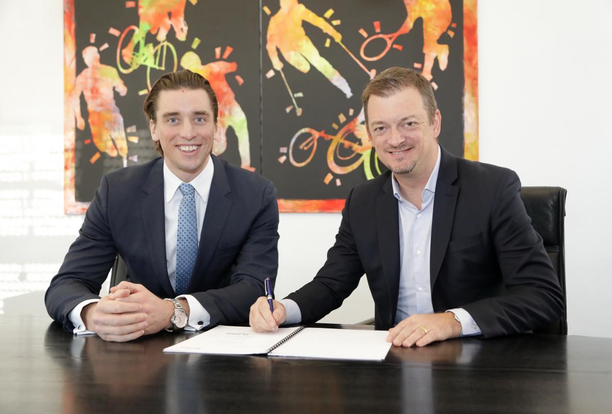 Two men smiling while one of the signs a contract