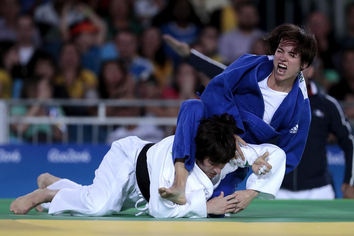 Female judoka Sandrine Martinet in a blue robe throws a judoka in a white robe onto the mat