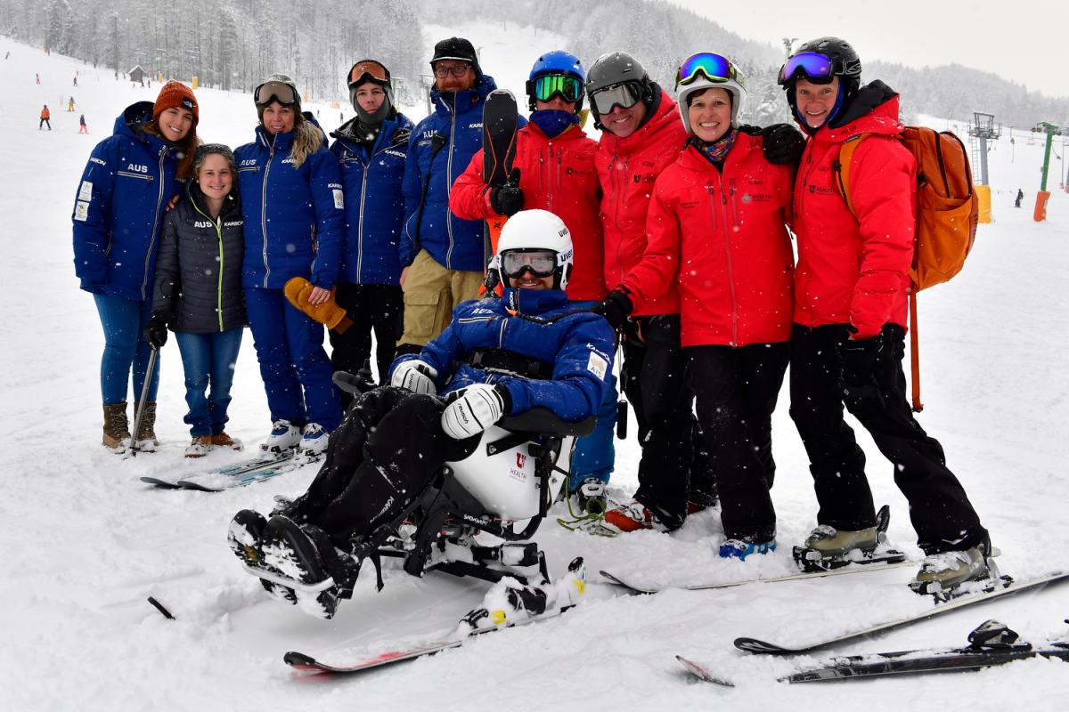 a group of skiing technical people standing behind a male Para alpine sit skier on the ski slope