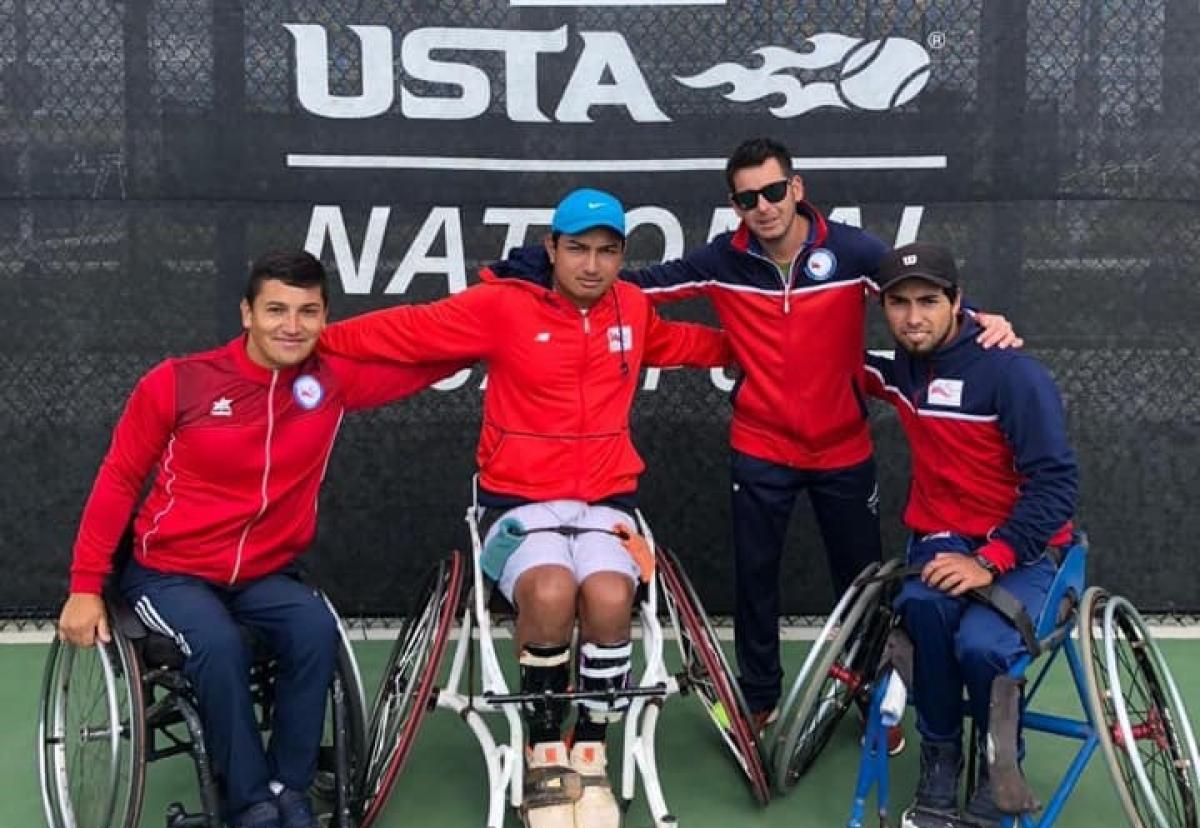 three male wheelchair tennis players and another man with their arms around eachother on a hard court