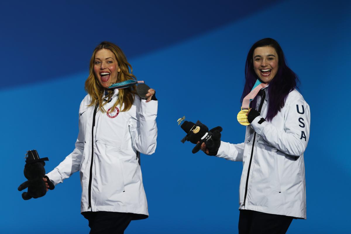 female Para snowboarders Amy Purdy and Brenna Huckaby holding up their medals and waving 