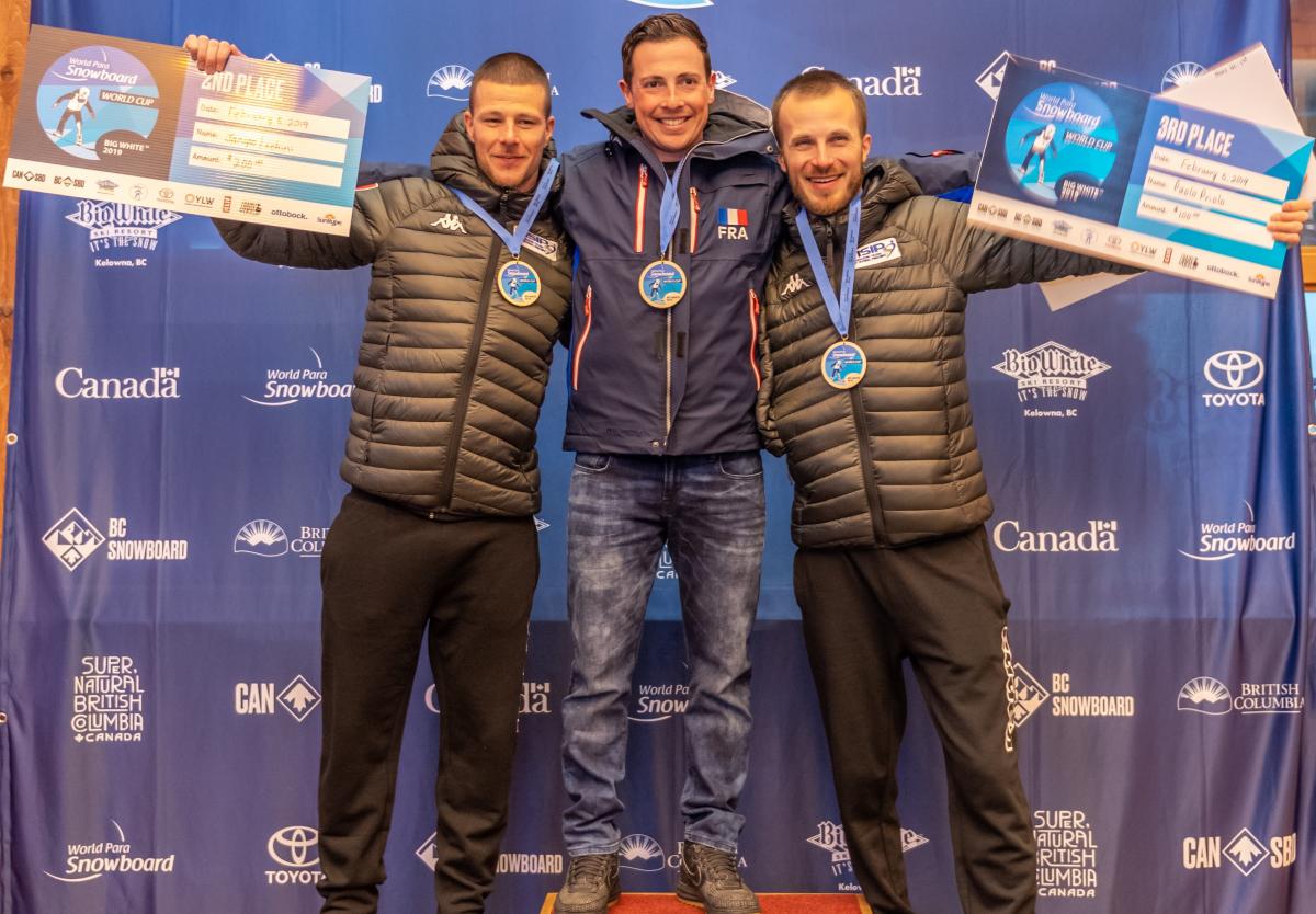 Maxime Montaggioni - Big White 2019 three male Para snowboarders with Maxime Montaggioni in the middle standing on the podium with their arms around eachother