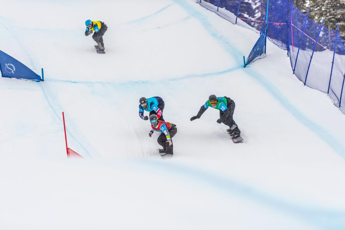 four male Para snowboarders racing on the snow with Alex Massie on the right