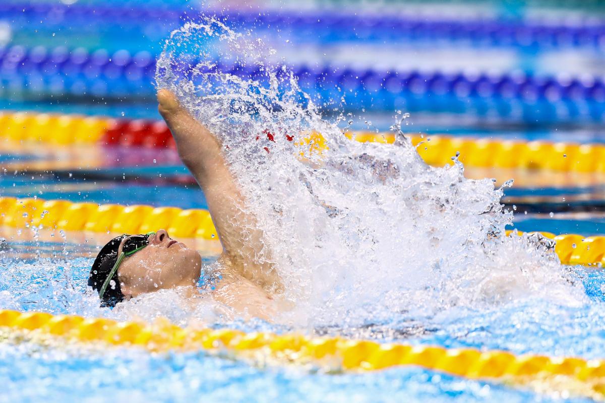 male Para swimmer Cameron Leslie lifts his arm up out of the water during a backstroke race