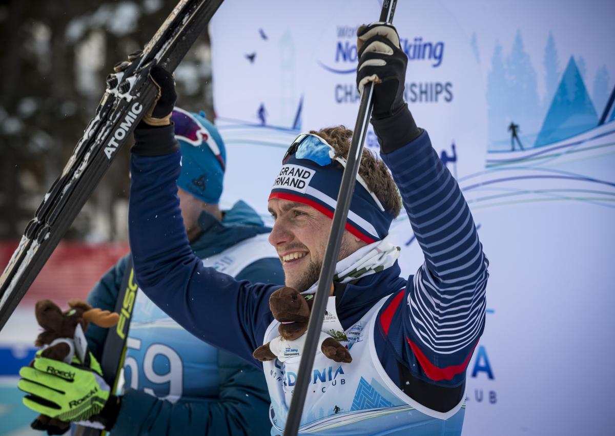 male Para Nordic skier Benjamin Daviet lifts up his skis in celebration on the podium