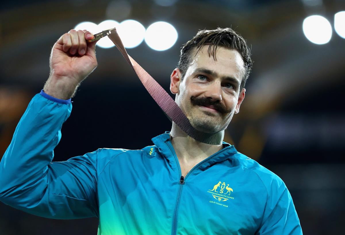 male Para sprinter Evan O'Hanlon holds up a gold medal on the podium