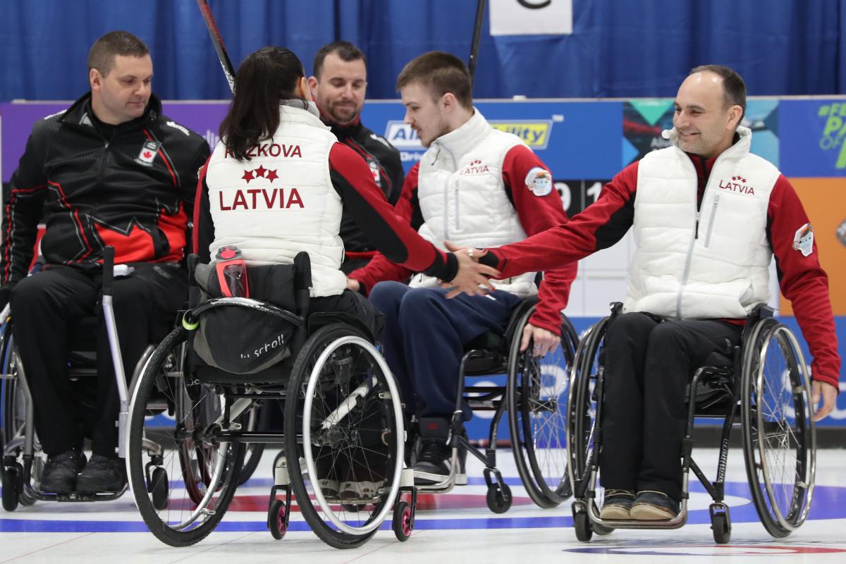 wheelchair curlers from Latvia high-five after beating Canada on the ice