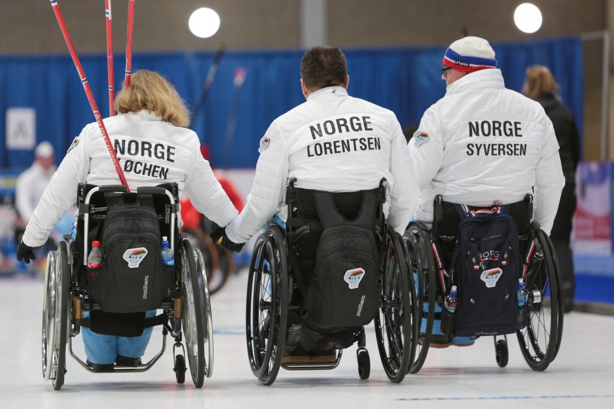 three wheelchair curlers with their backs to the camera with Norway on their jackets