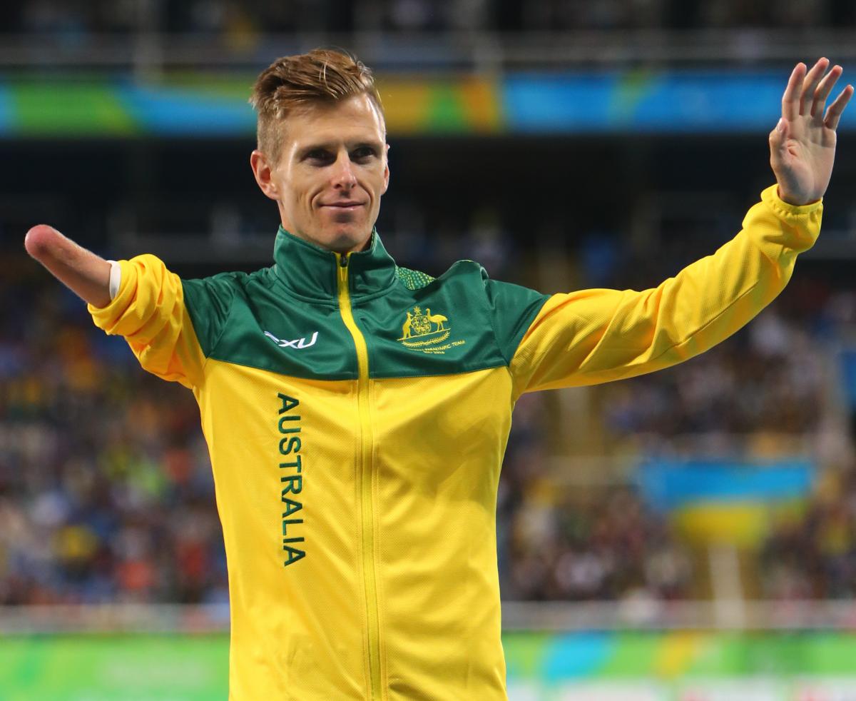 male Para athlete Michael Roeger raises his arms on the podium