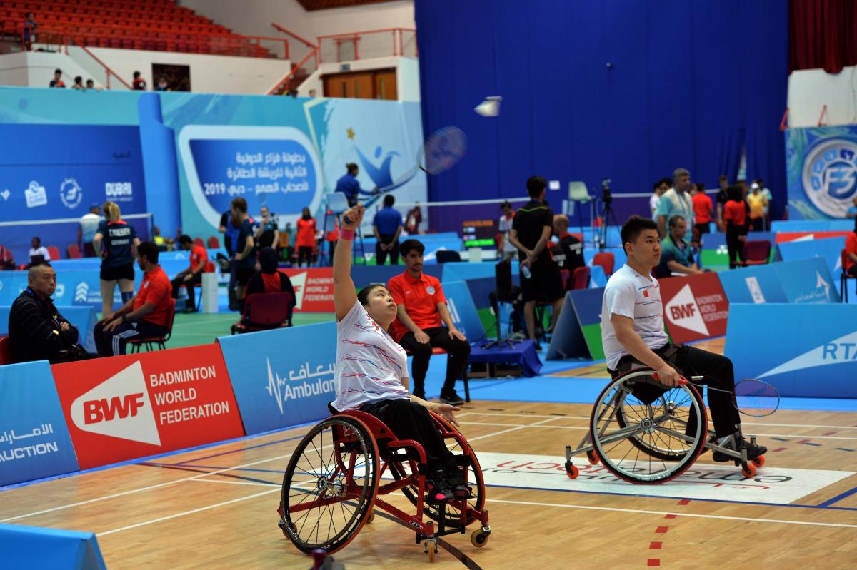 male and female Chinese Para badminton players in wheelchairs playing on the court