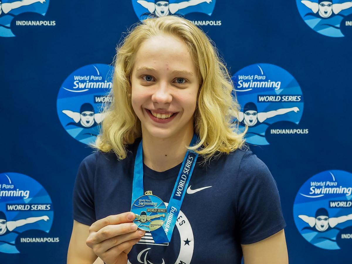 female Para swimmer Julia Gaffney smiles and holds up a gold medal