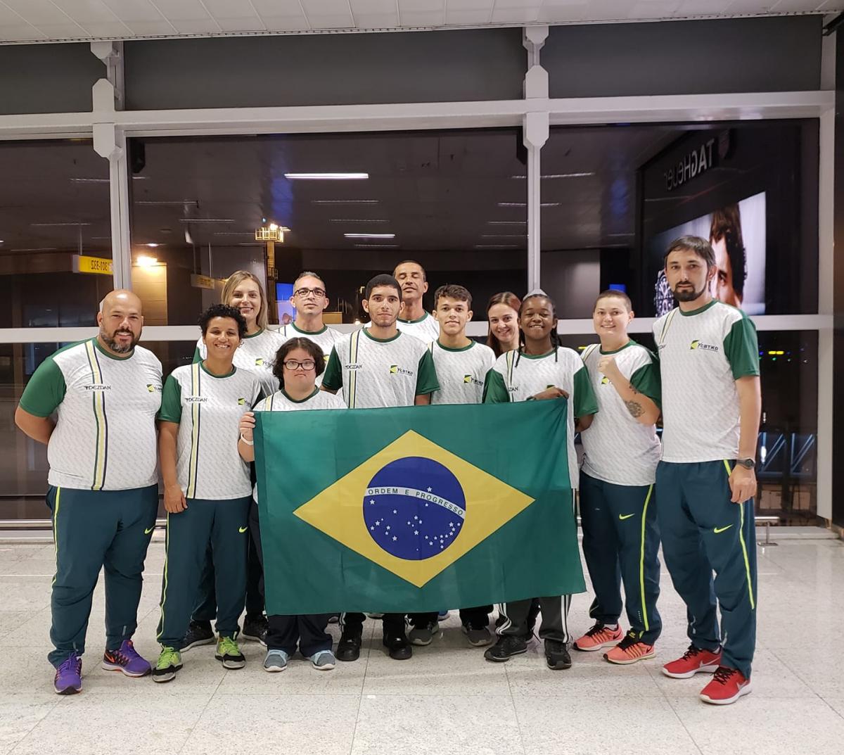 female Para taekwondo fighter Debora Menezes with other fighters holding a Brazilian flag