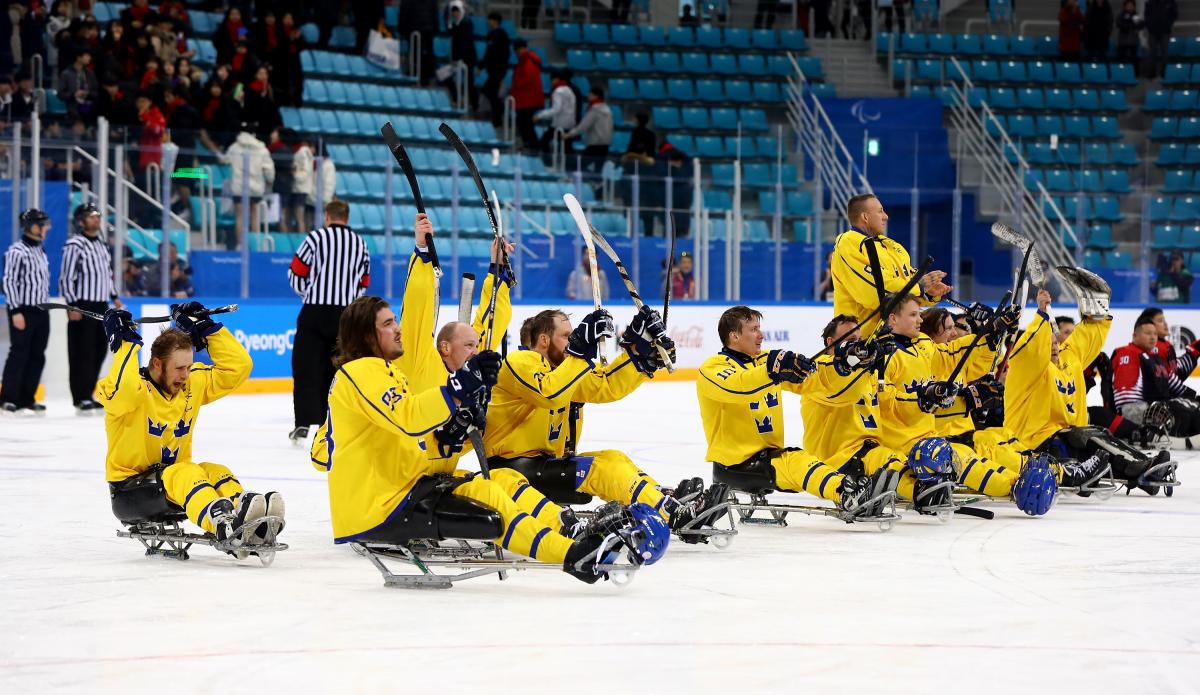 the Sweden Para ice hockey team raise their sticks in celebration on the ice
