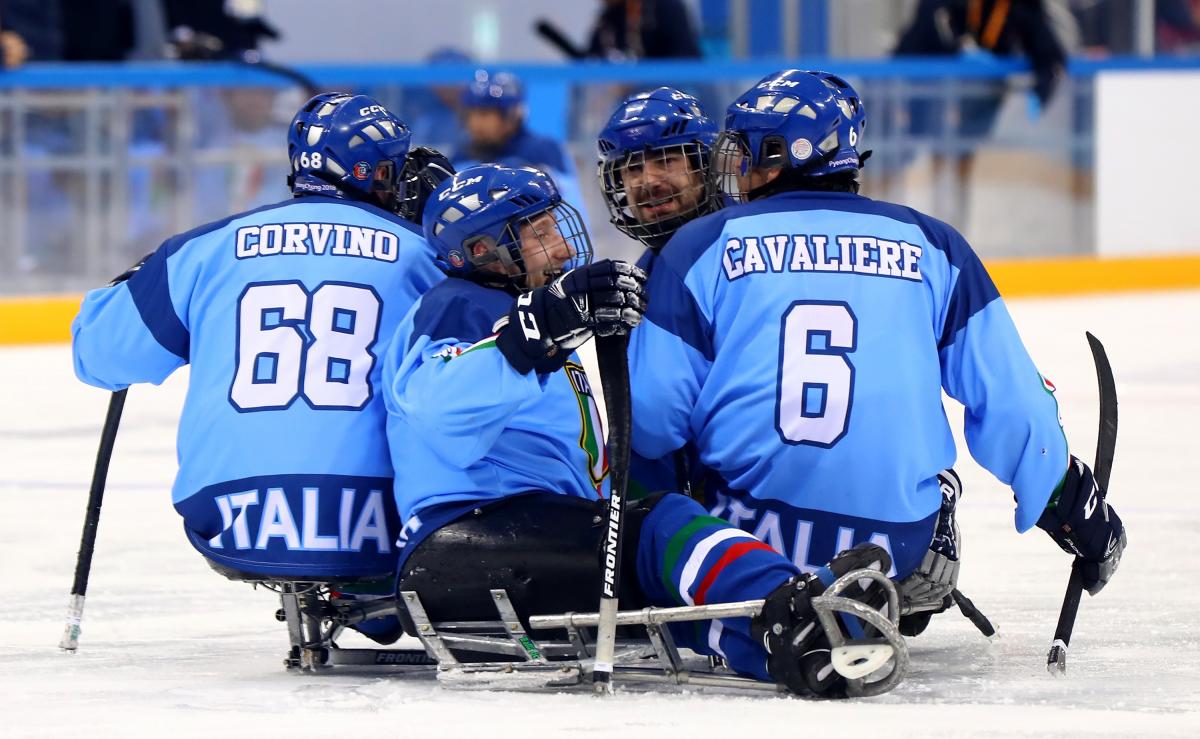 male Para ice hockey player Nils Larchi being hugged on the ice by his teammates