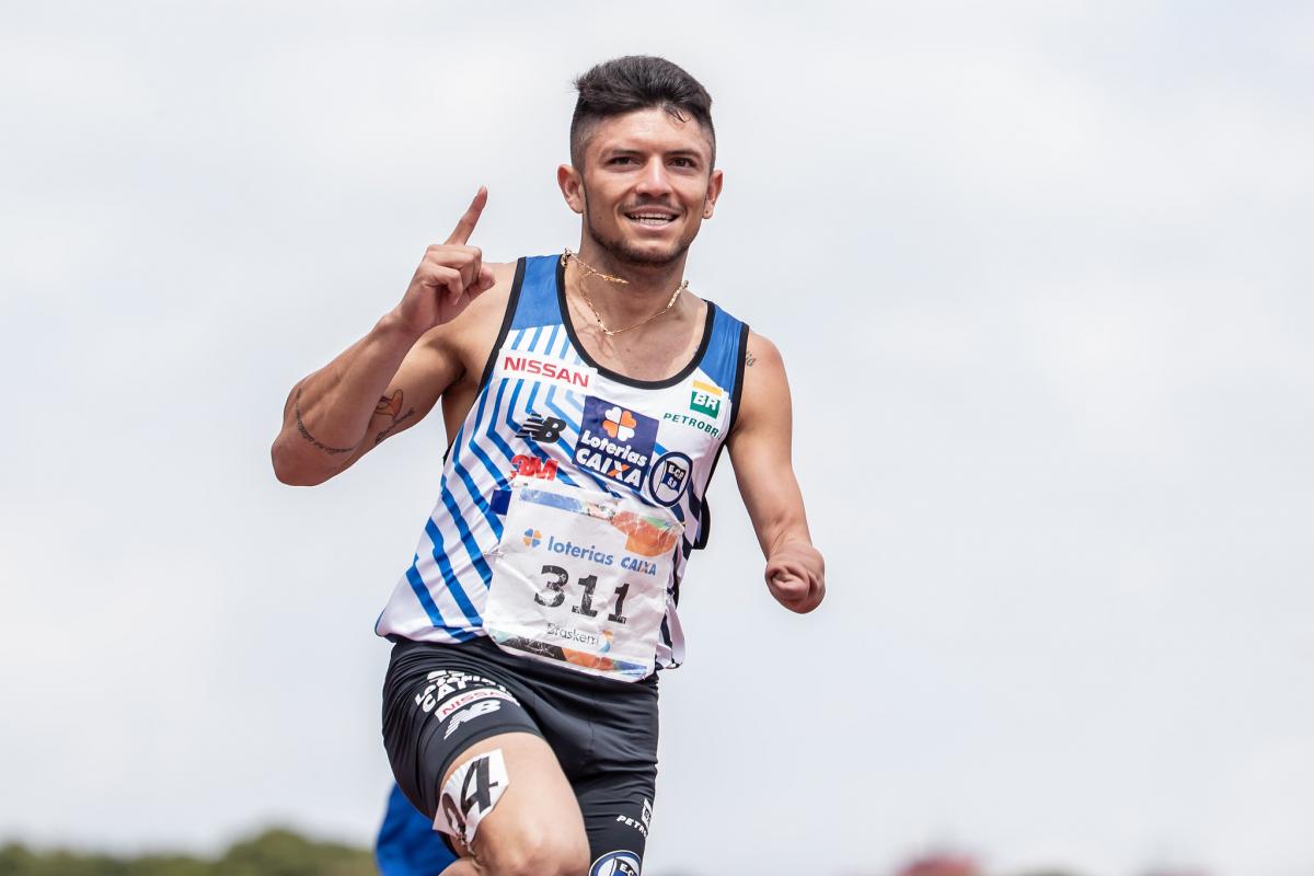 male Para athlete Petrucio Ferreira raises his finger as he crosses the finish line 