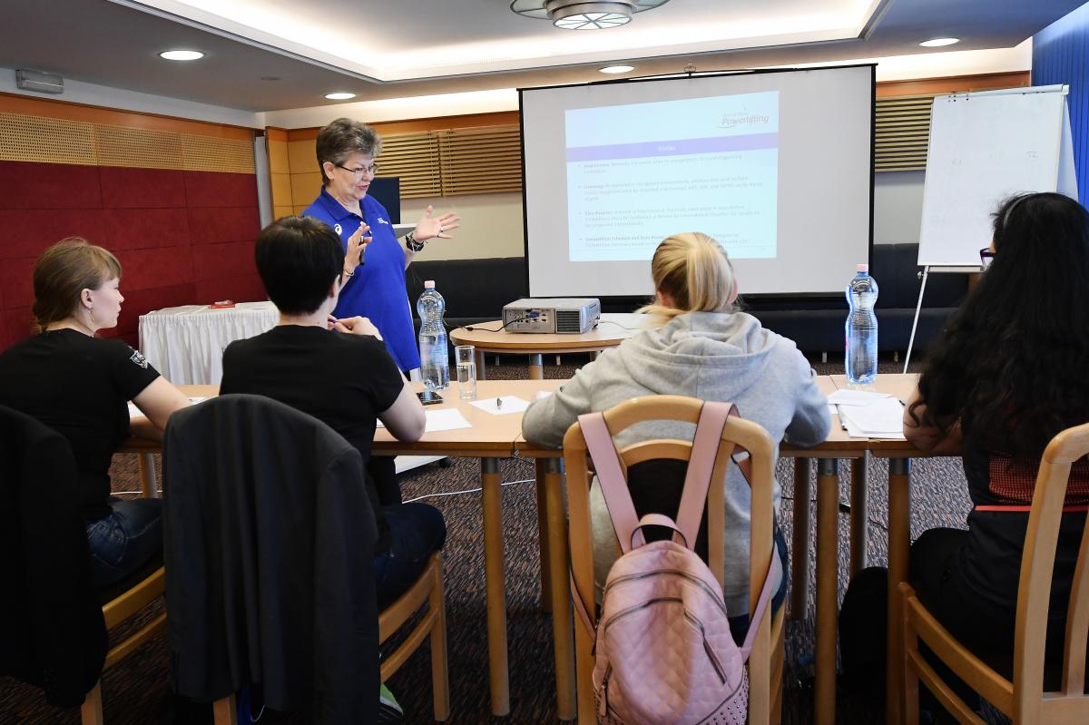 Course educator standing in front of course participants who are taking notes and staring ahead at the screen