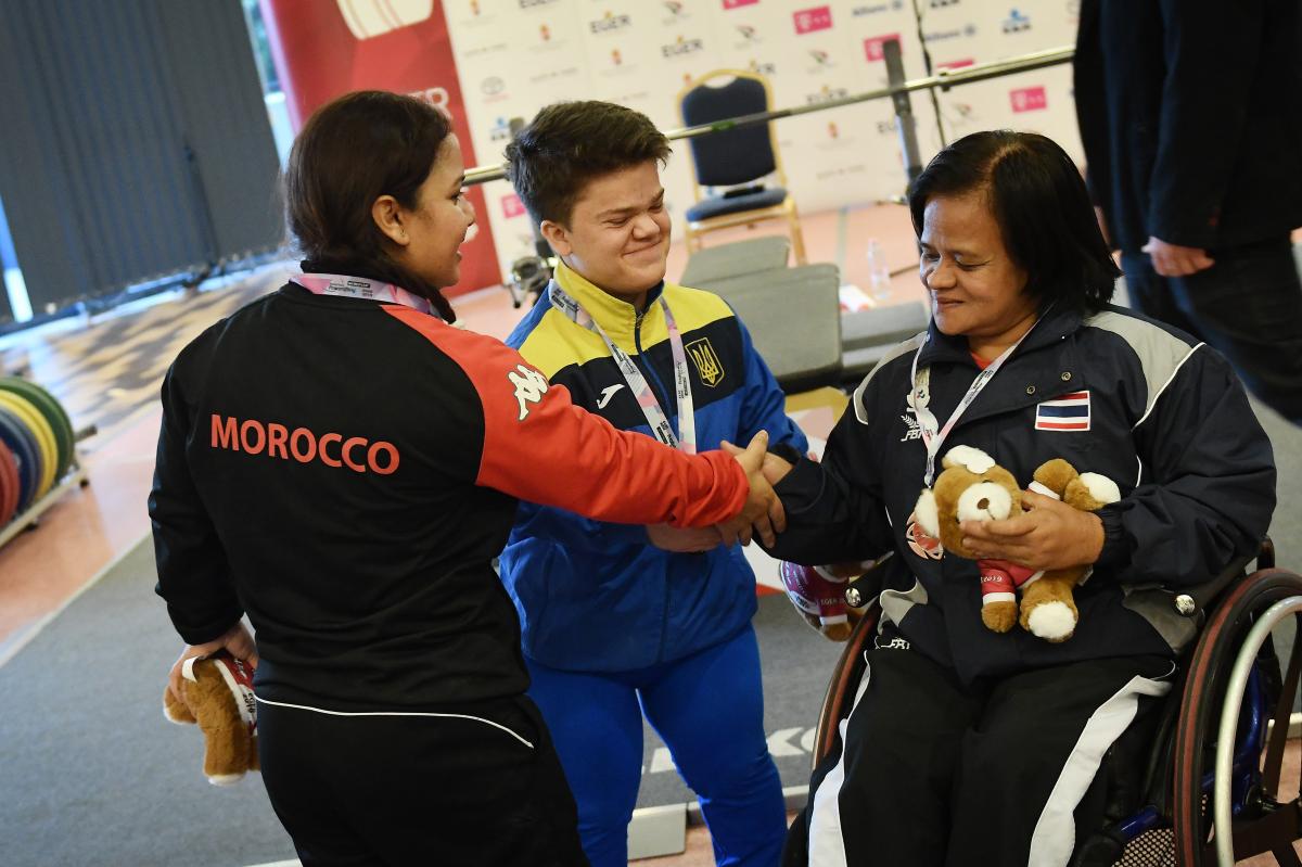 three female powerlifters shaking hands together on the podium