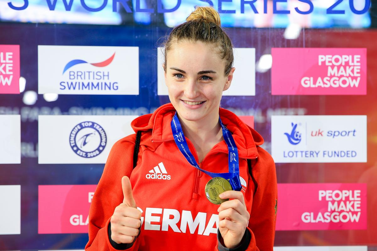 female Para swimmer Elena Krawzow gives a thumbs up and holds up her gold medal 