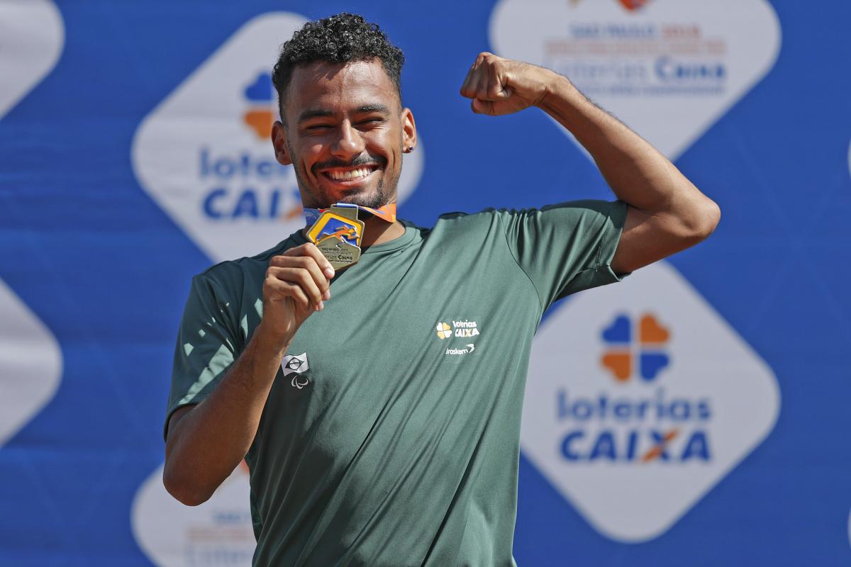 male Para athlete Daniel Martins holds up his arm and fist pumps while holding a gold medal and smiling