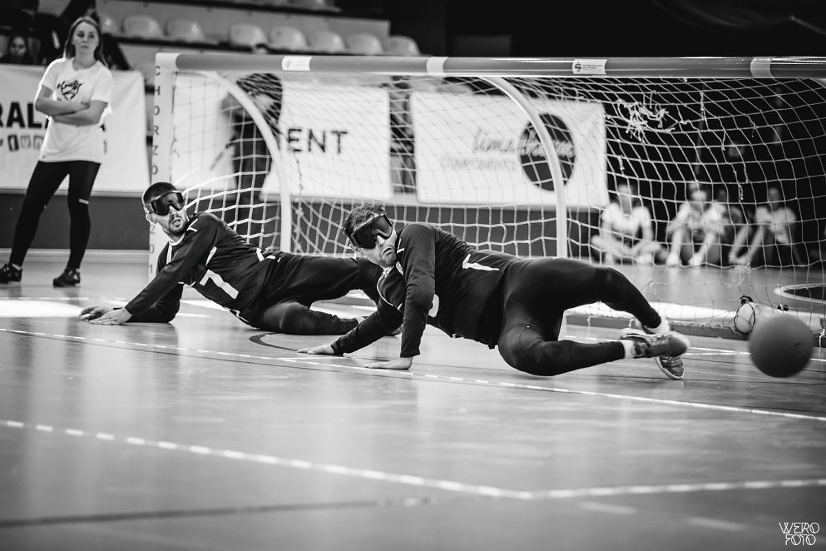 a team of male goalball players standing with their arms linked on a court