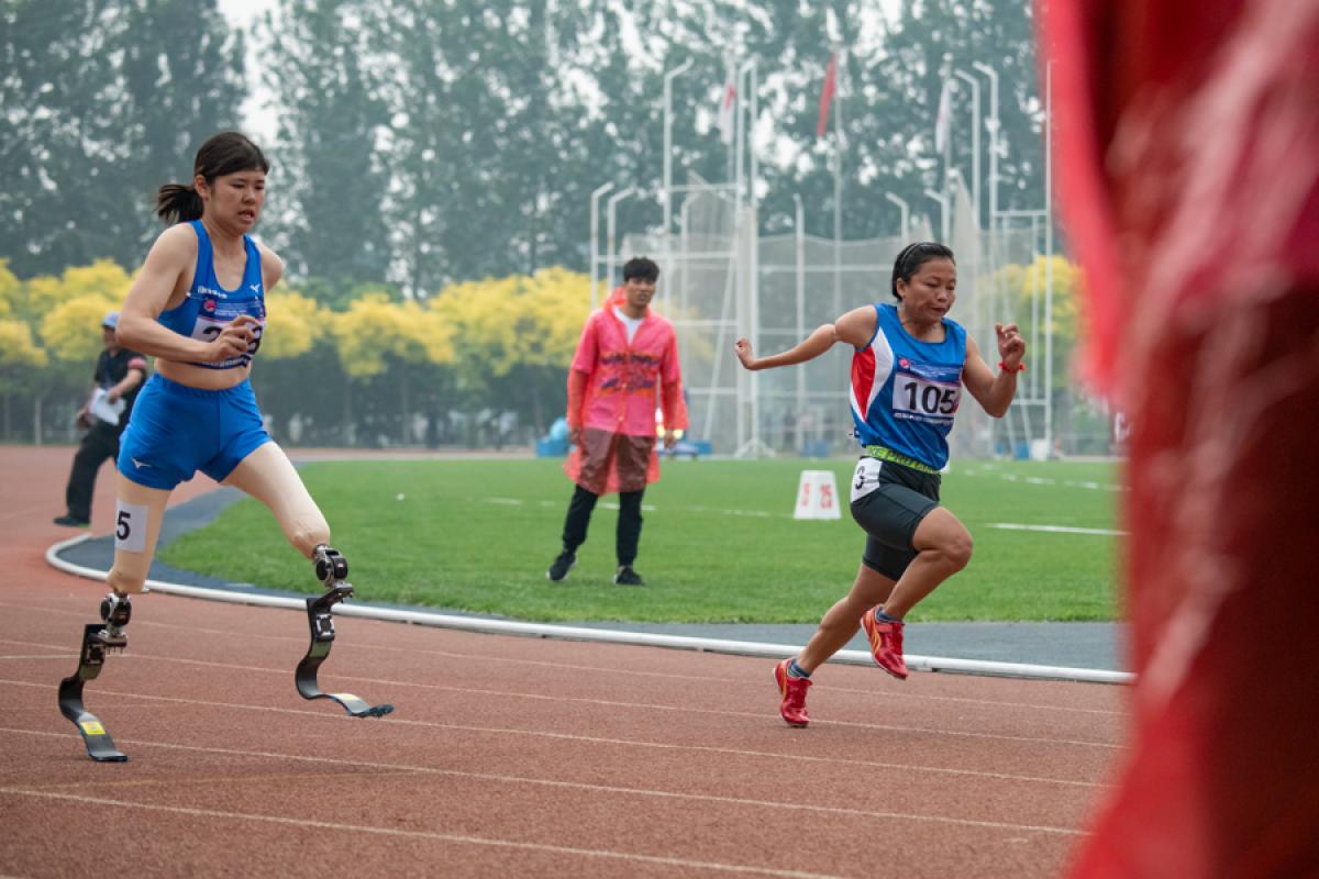 A double-leg amputee woman running against another woman on an athletics track