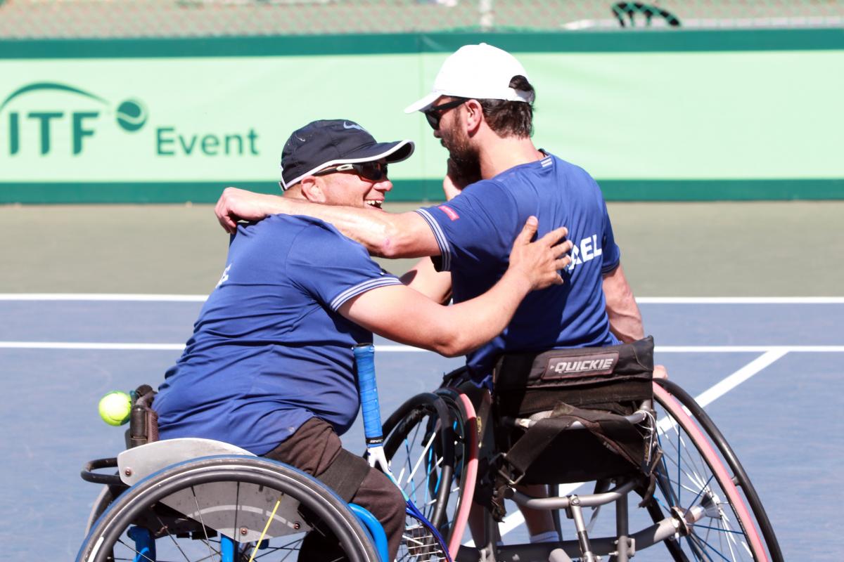 two male wheelchair tennis players from Israel hug on a hard court 