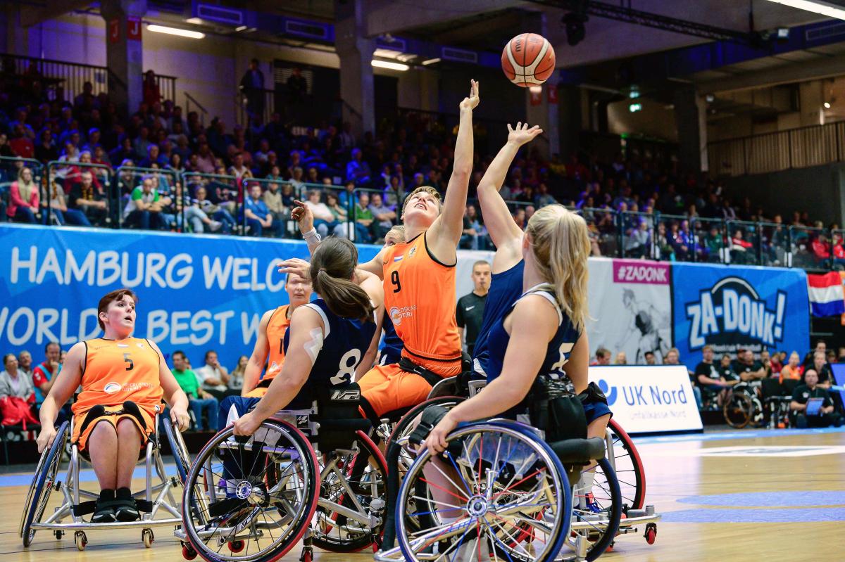 female wheelchair basketball players from Netherlands and Great Britain reaching up for the ball