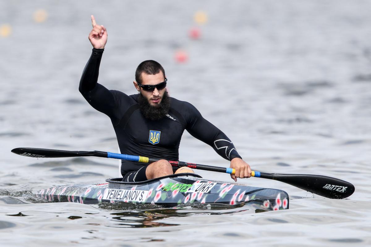 Serhii Yemelianov celebrates in the canoe with his hand in the air after winning gold