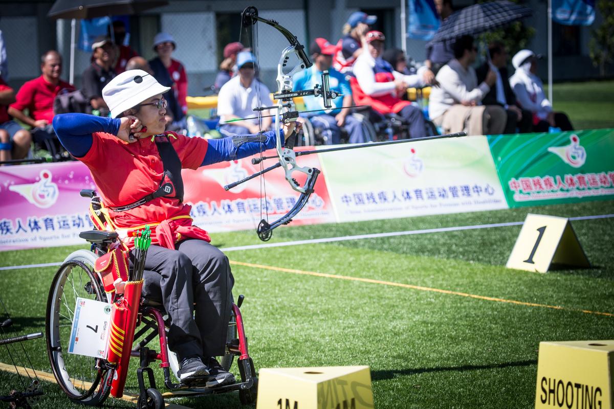 Chiense female archer in a wheelchair pulls back on her bow string