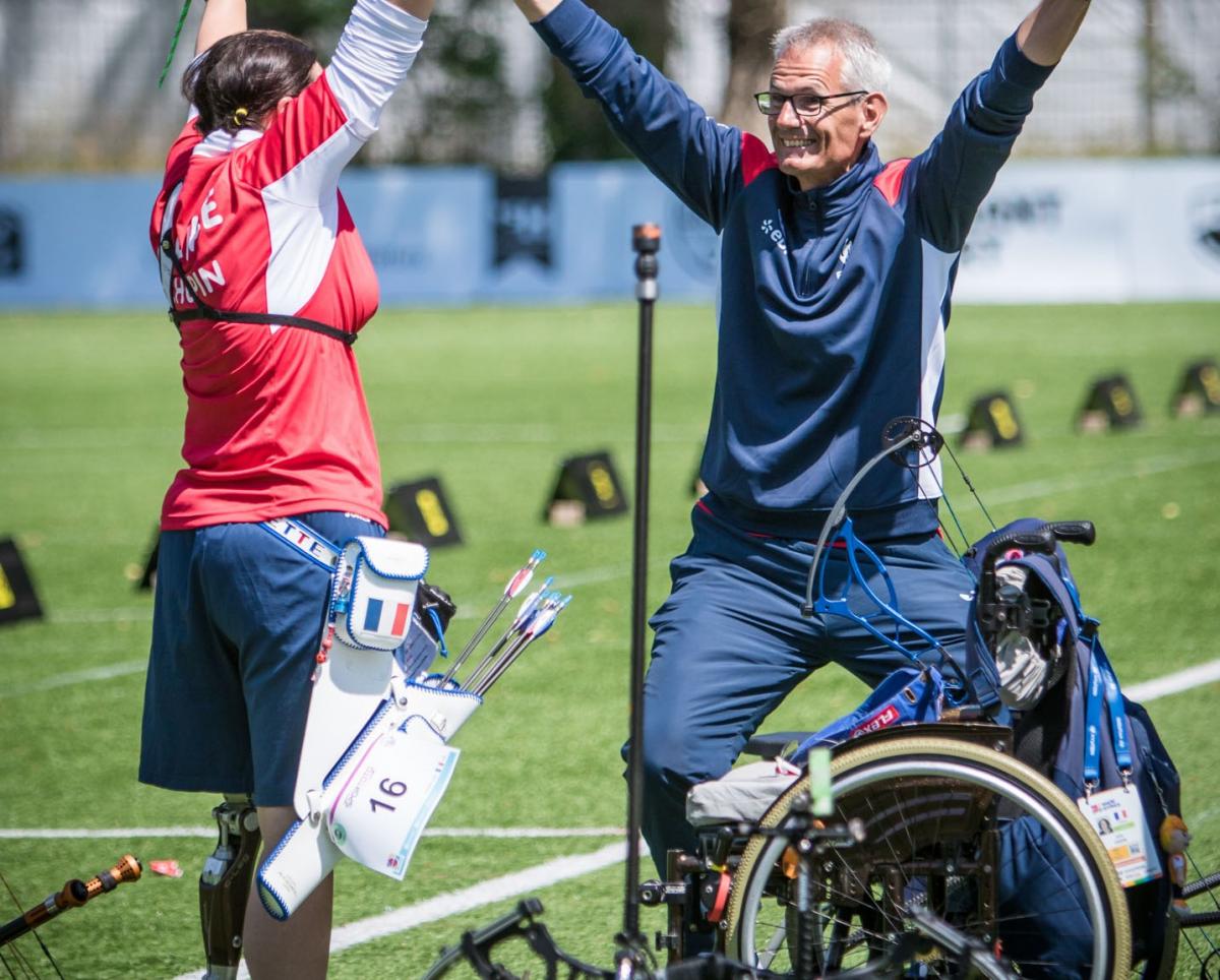 female Para archer Julie Chupin raises her arms in celebration with her coach