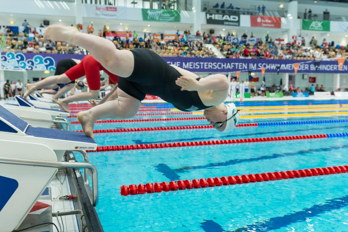 Ellie Simmonds - Great Britain - Berlin 2019 Para Swimming World Series A short stature female swimmer jumping in the water in front of other swimmers