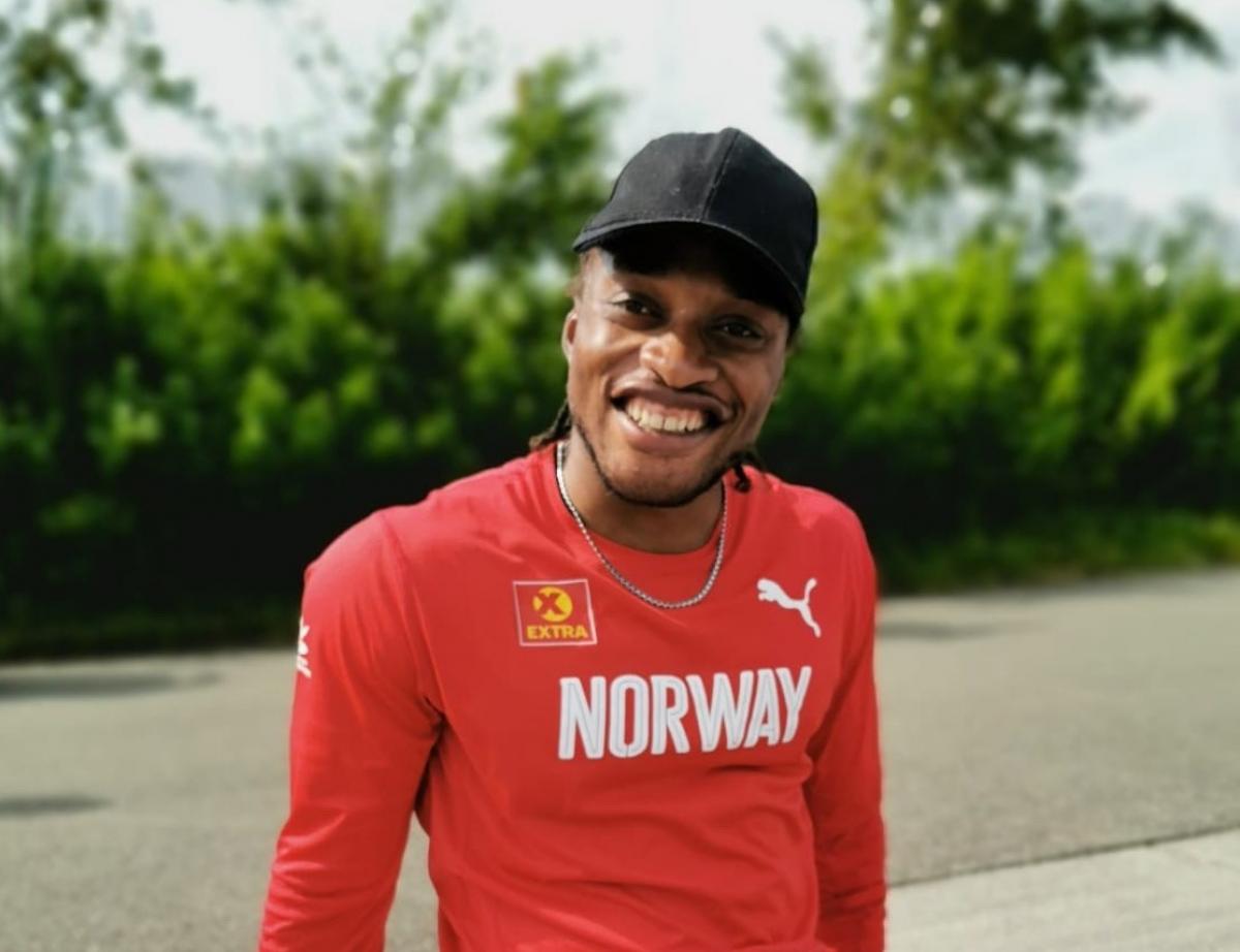 A man with a shirt a long-sleeved red shirt written Norway seated on the sidewalk