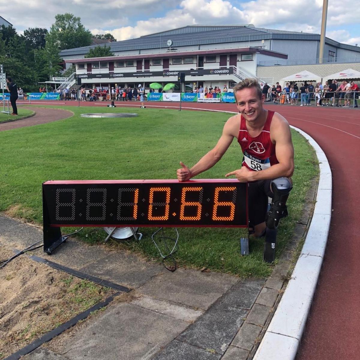 German male sprinter poses next to a clock that says 10.66