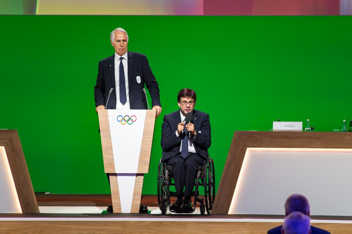 A man standing and another man in a wheelchair on stage