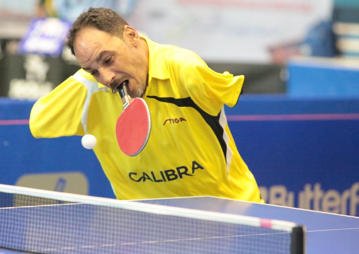 Egyptian male table tennis player holds racket in mouth and attempts to hit the ball