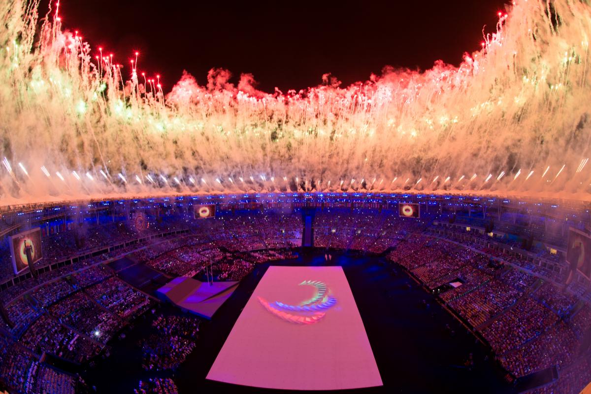 a high shot of the Olympic Stadium in Rio with fireworks going off and the Agitos symbol on the floor