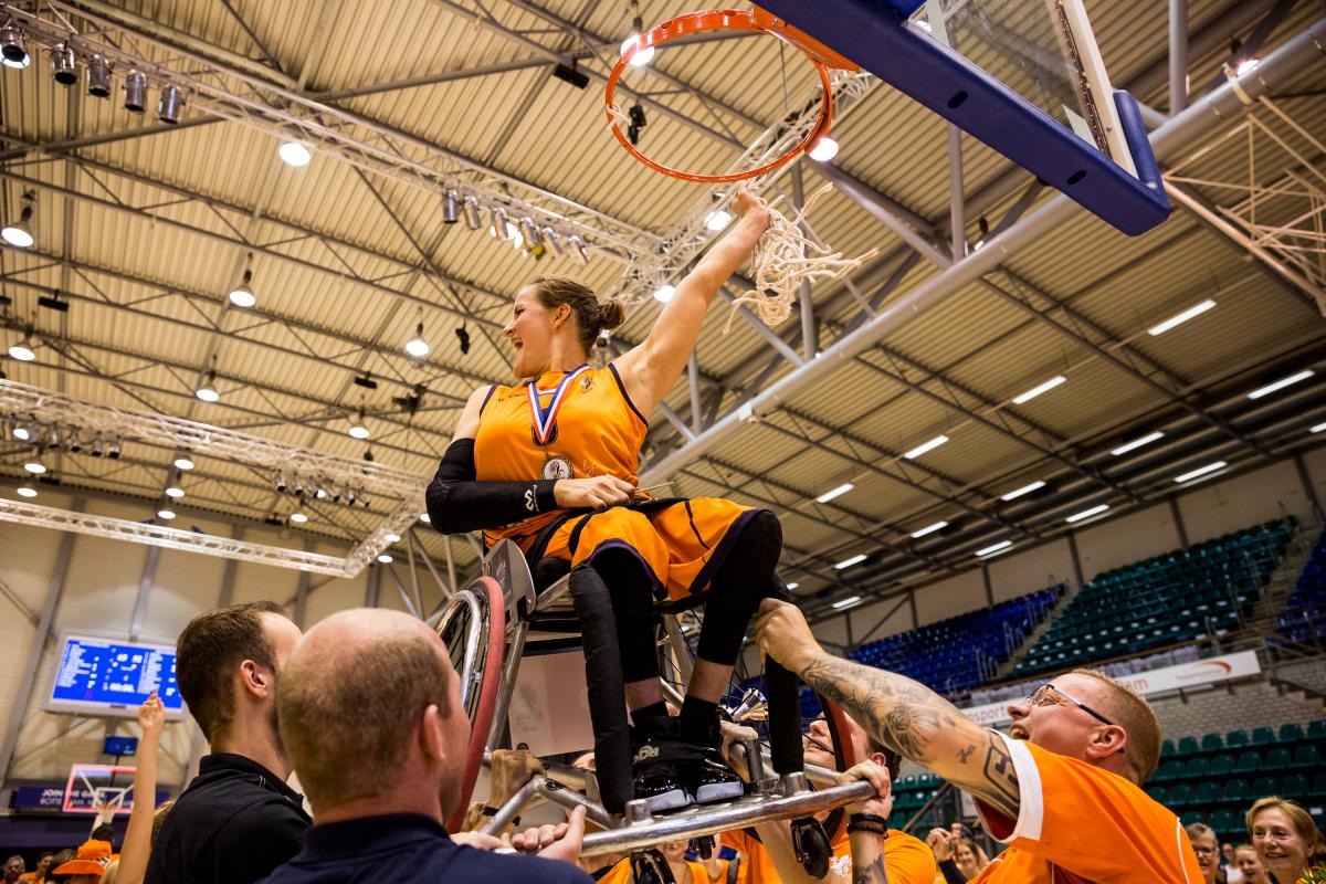 Dutch female being lifted up on her wheelchair to the basketball hoop
